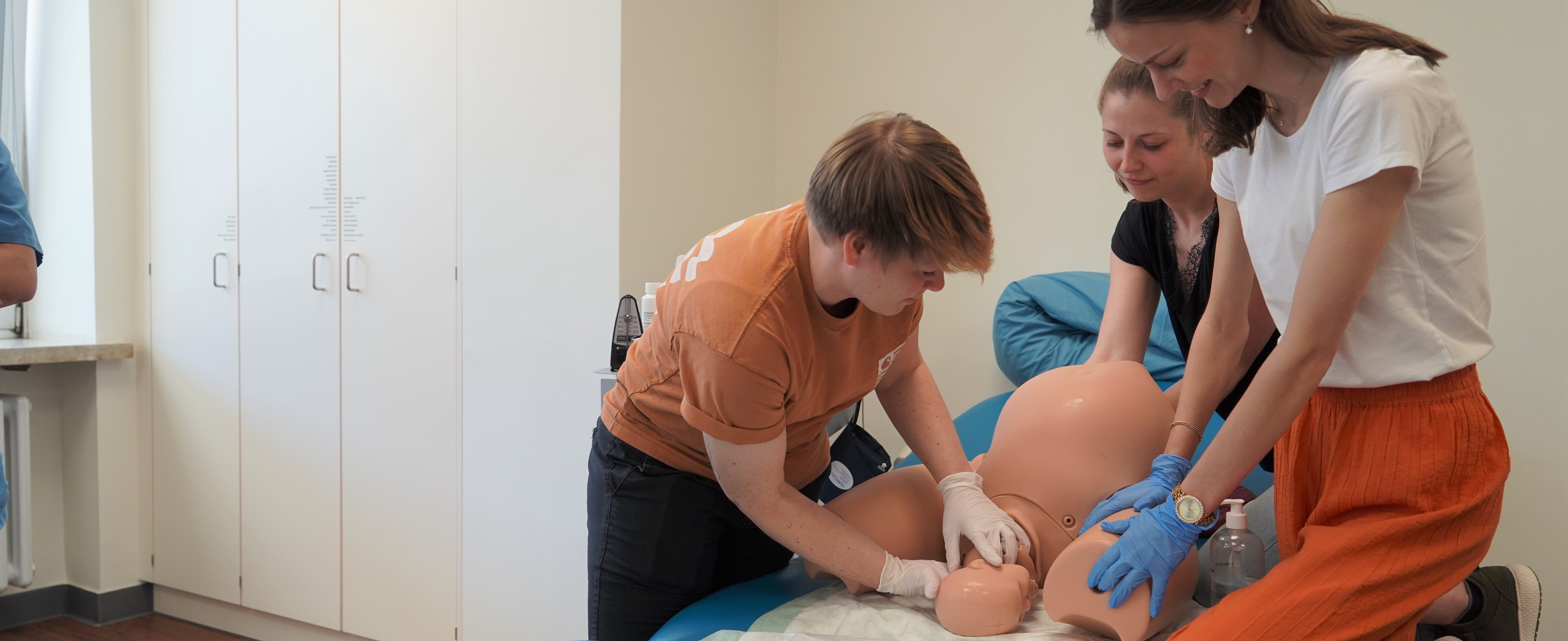 Drei Hebammenstudierende stehen um den Geburtssimulator und simulieren eine Geburt.