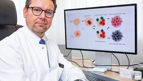 A man sits at a desk and looks at a schematic representation of the development of blood cancer on a computer screen.