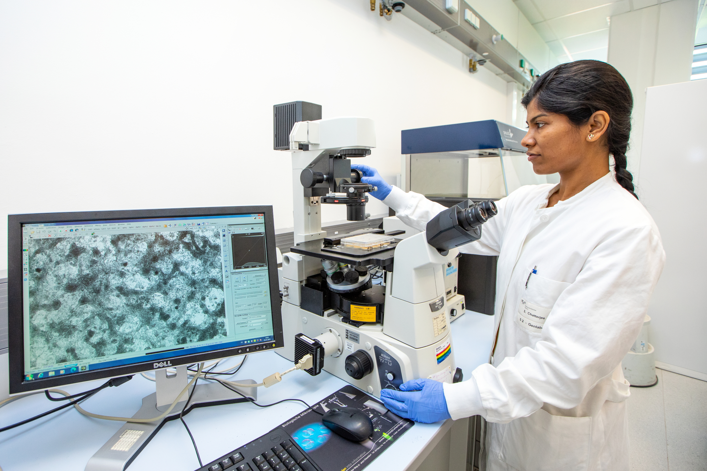 Dr Shambhabi Chatterjee stands in the laboratory in front of a screen showing heart muscle cells.