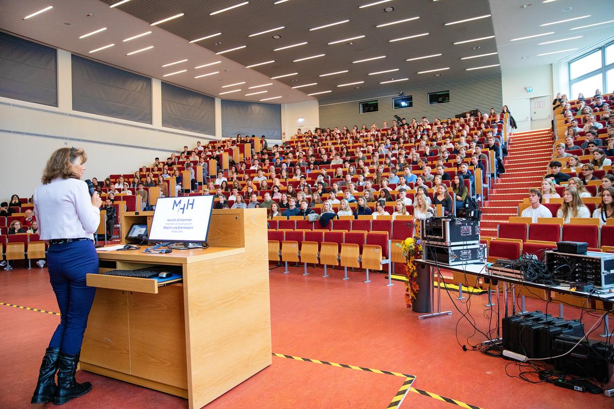 Copyright: Karin Kaiser / MHH Blick vom Rednerpult in einen vollen Hörsaal. Links steht MHH-Präsidentin Denise Hilfiker-Kleiner und spricht zu den Erstsemester.