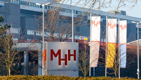 Aufnahme des Einfahrtsbereiches der MHH mit großem MHH-Logo und drei gehissten Fahnen mit MHH-Logo.