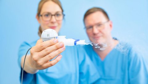 A doctor holds an inhaler in her hand, to her right a doctor looks at the device.