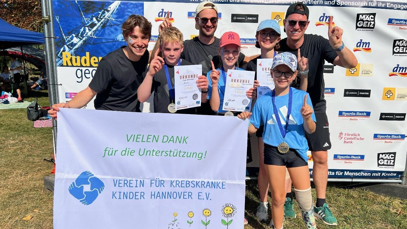 Mehrere Personen, darunter Kinder, stehen für eine Gruppenfoto zusammen und jubeln in die Kamera. 