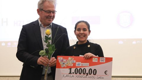 Ximena León Lara is standing next to Prof Reinhold Förster from RESIST, holding a large sign with the amount of 1000 euros on it.