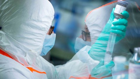 A woman wearing a face mask and special clothing holds utensils used to manufacture a drug.