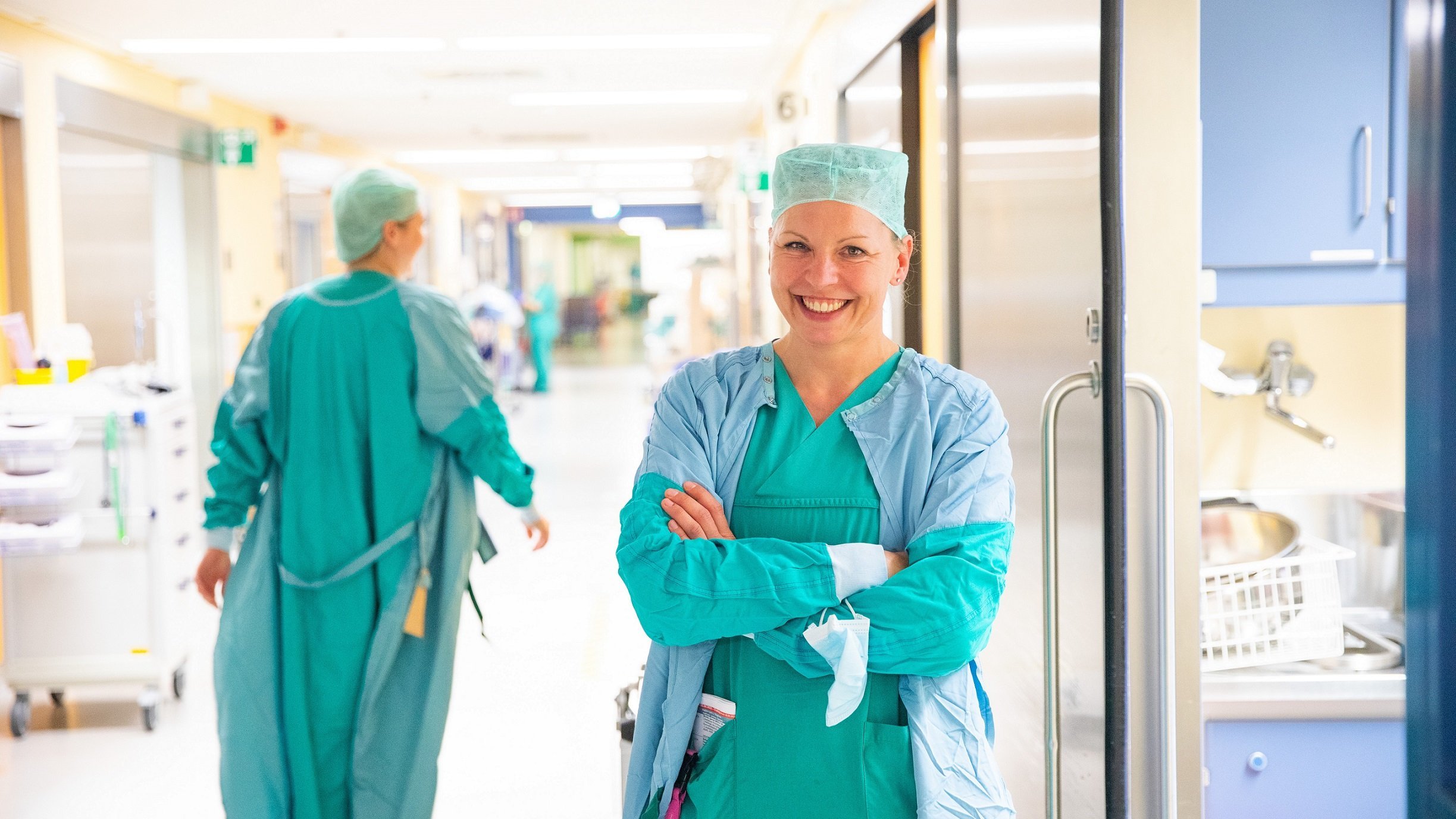 Marieke Jüttner stands in surgical clothing in a corridor at MHH.