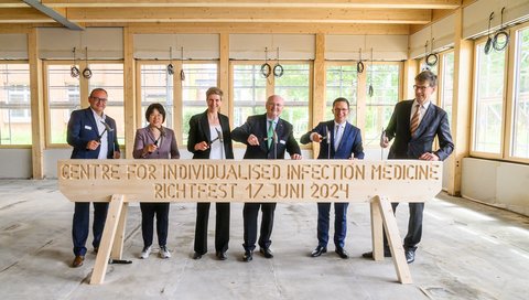 Markus Cornberg, CiiM Director; Yang Li, CiiM Director; Jennifer Debarry, CiiM Coordinator; Michael Manns, President of the MHH; Falko Mohrs, Lower Saxony Minister for Science & Culture; Christian Scherf, Admin. Managing Director of the HZI, stand at a long wooden beam and hammer nails into the wood. 
