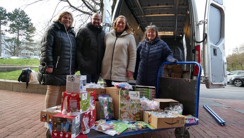 Vier Personen stehen vor einem Transportwagen voll mit eingepackten Geschenken. 