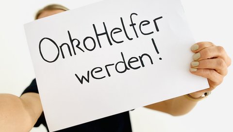 Eine Frau hält ein Plakat mit dem Schriftzug „OnkoHelfer“ hoch.