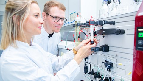 A man and a woman are standing in front of a chromatograph.