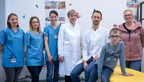 A ten-year-old boy sits on a treatment couch, surrounded by his mother and a study team.