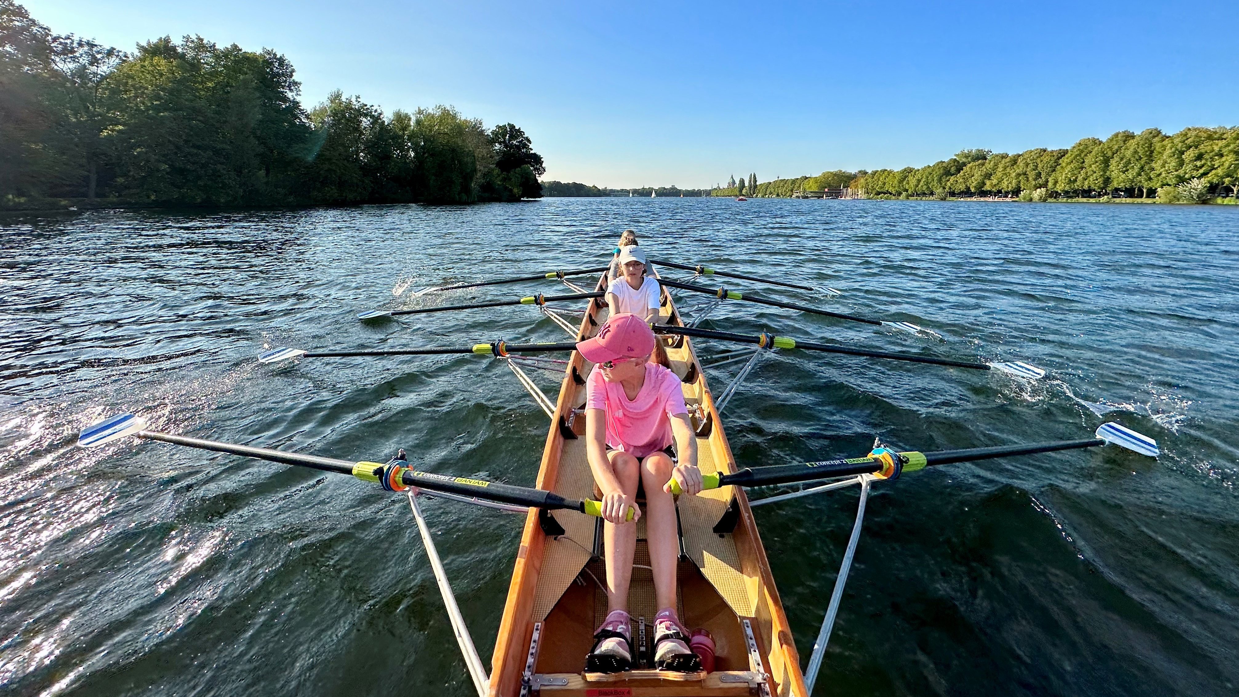 Ein Ruderboot mit vier Kinder fährt auf einem See. 