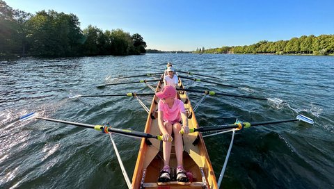 A rowing boat with four children is on a lake.