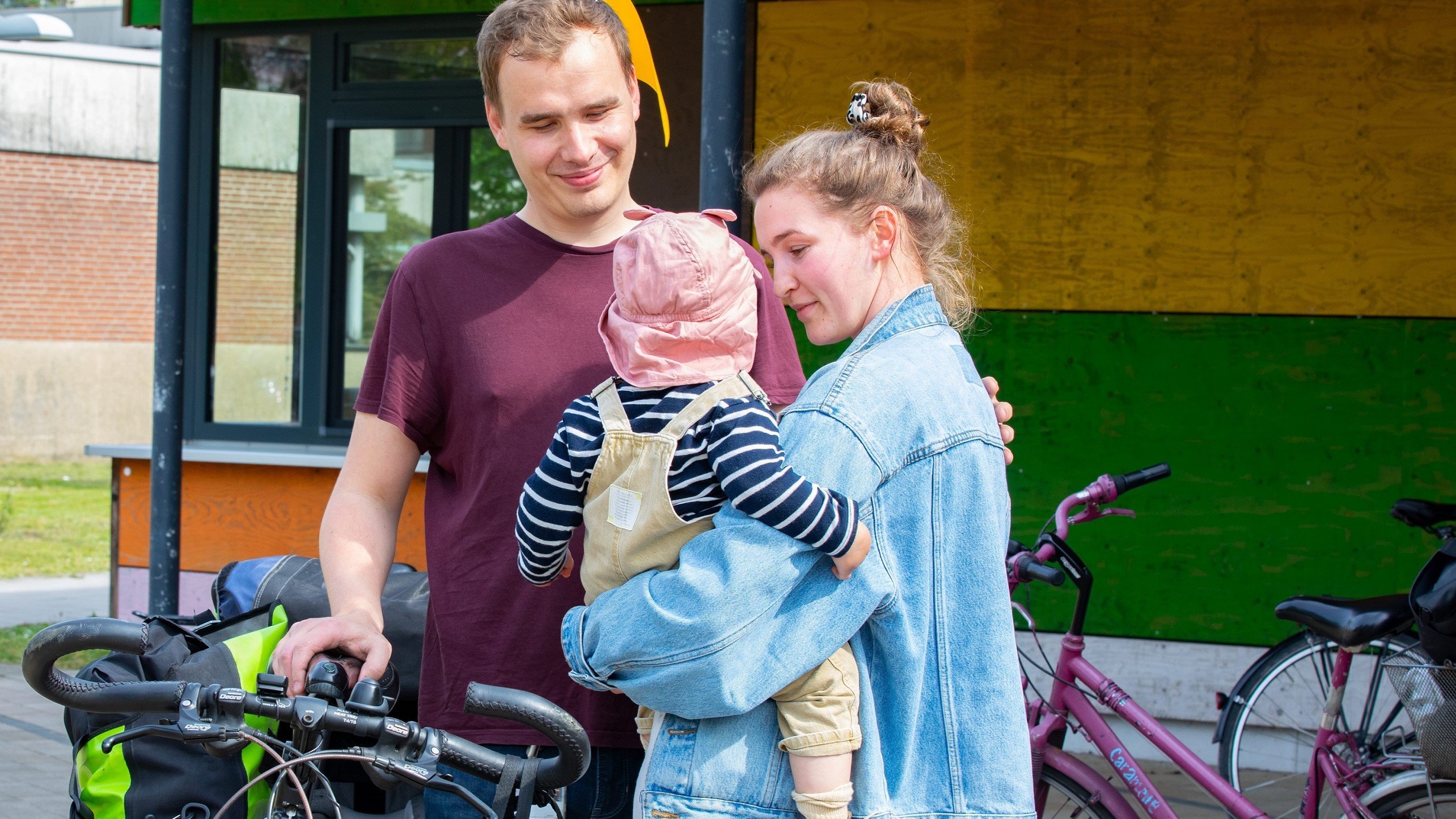 A woman carries a small child in her arms, a man stands next to her and looks at the child.