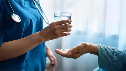 A medical assistant hands an older person a glass of water.