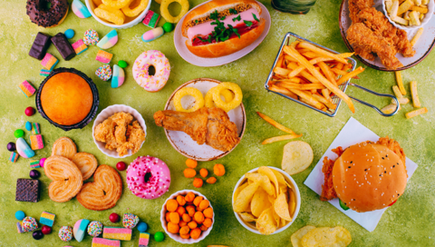  Many unhealthy foods such as doughnuts, chips, wine gums and burgers are served on a green surface. 