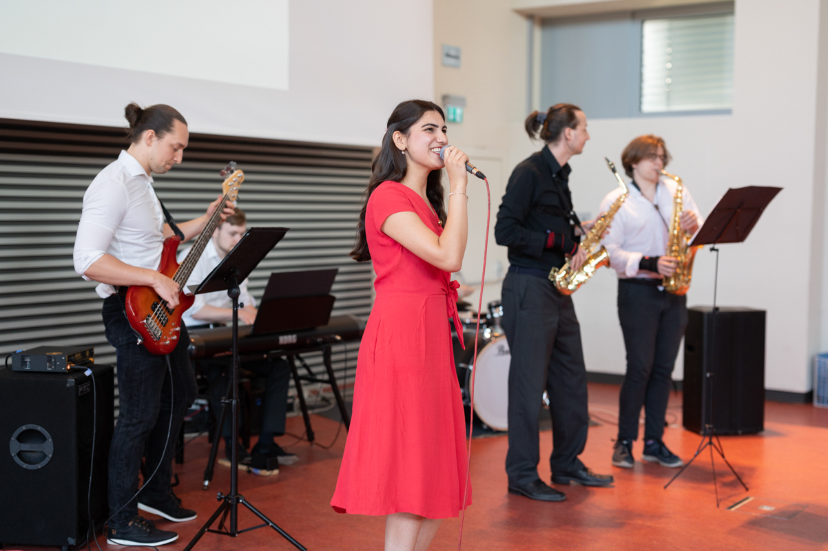 Die Band musiziert auf der Bühne, im Vordergrund ist die Sängerin in einem roten Kleid zu sehen.