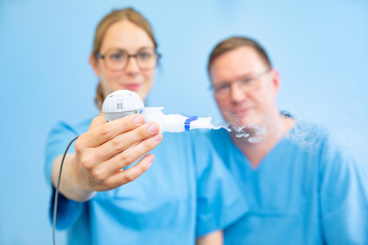 A doctor holds an inhaler in her hand, to her right a doctor looks at the device.