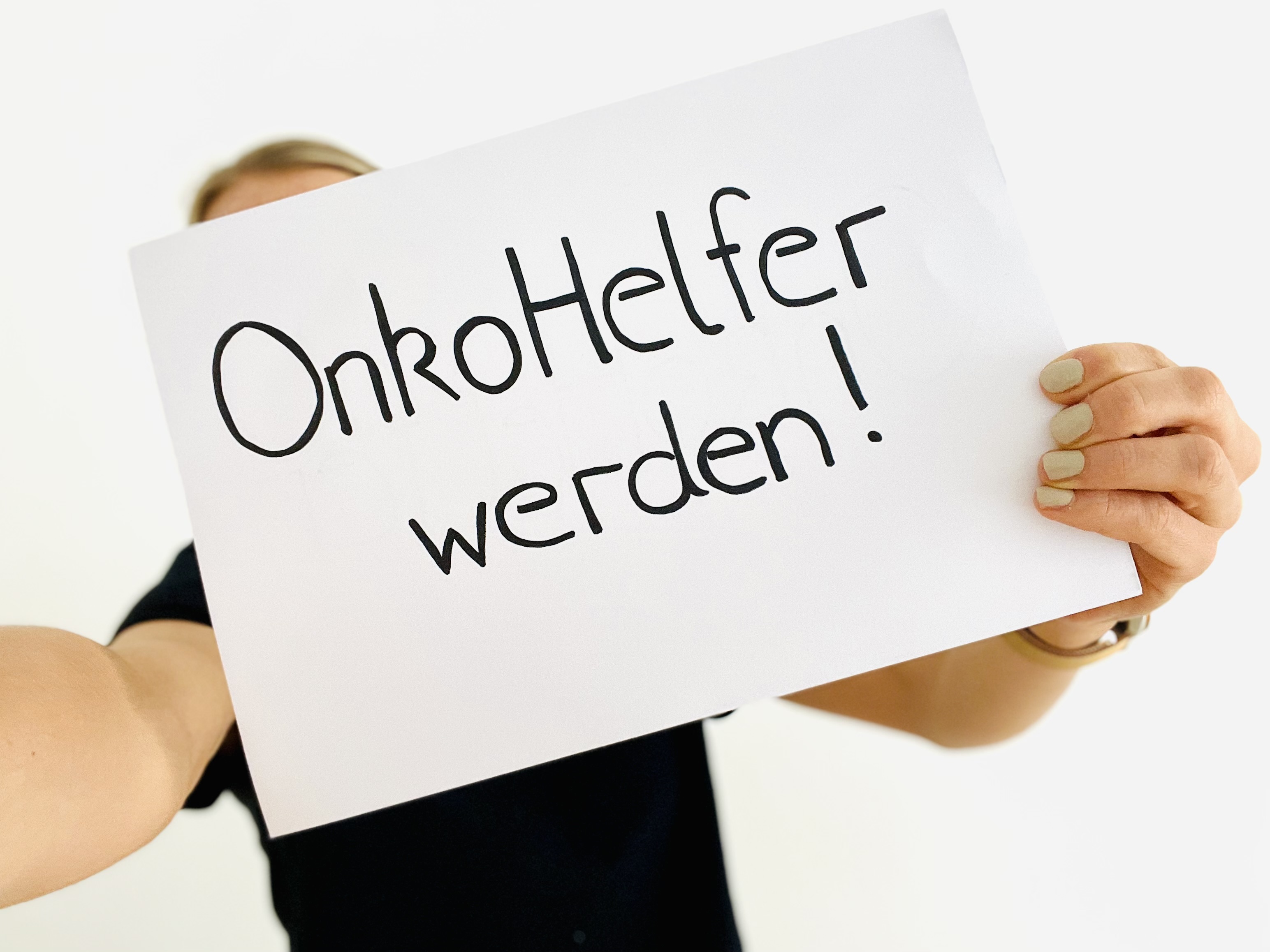 Eine Frau hält ein Plakat mit dem Schriftzug „OnkoHelfer“ hoch.