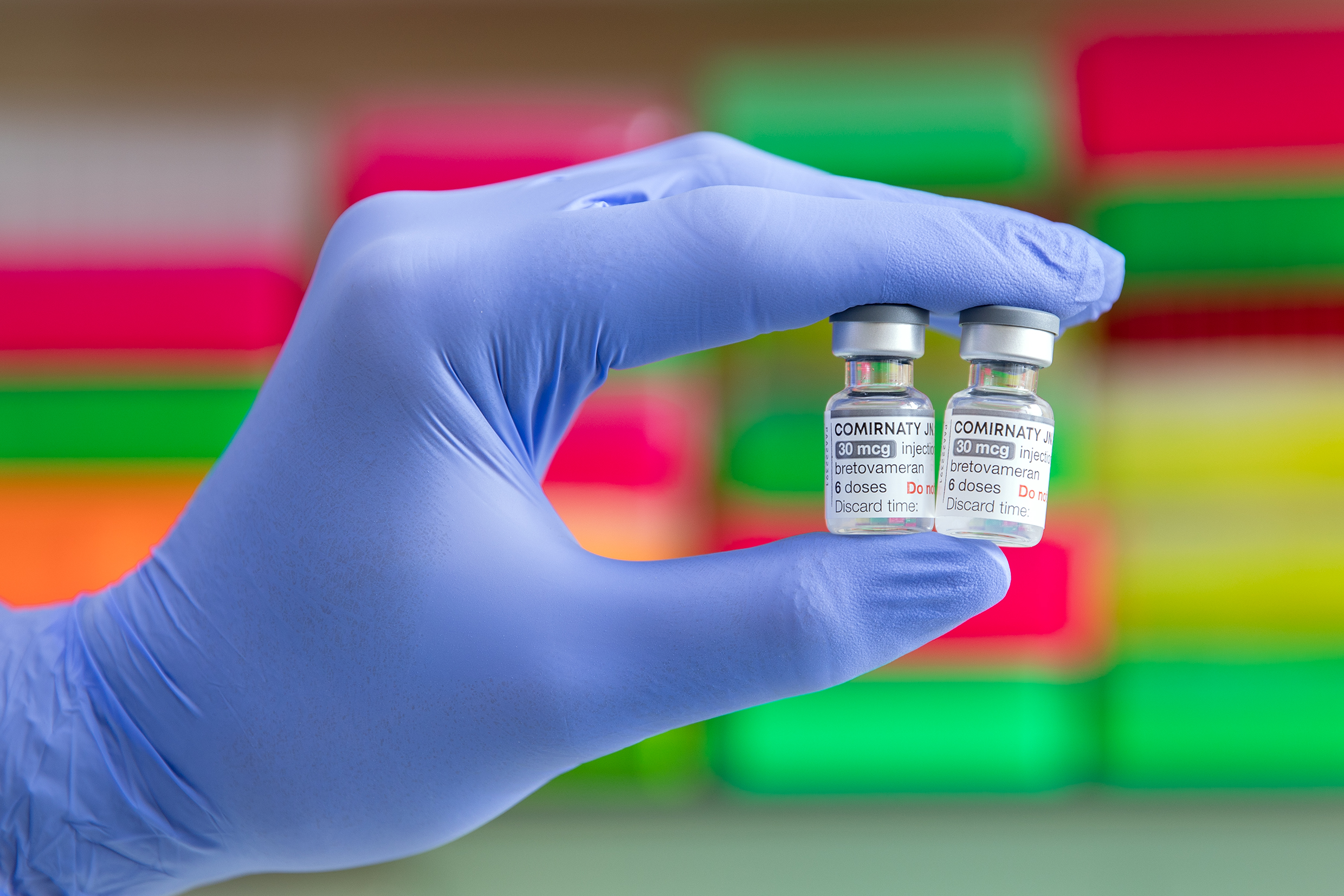 A hand holds two small bottles of coronavirus vaccine.