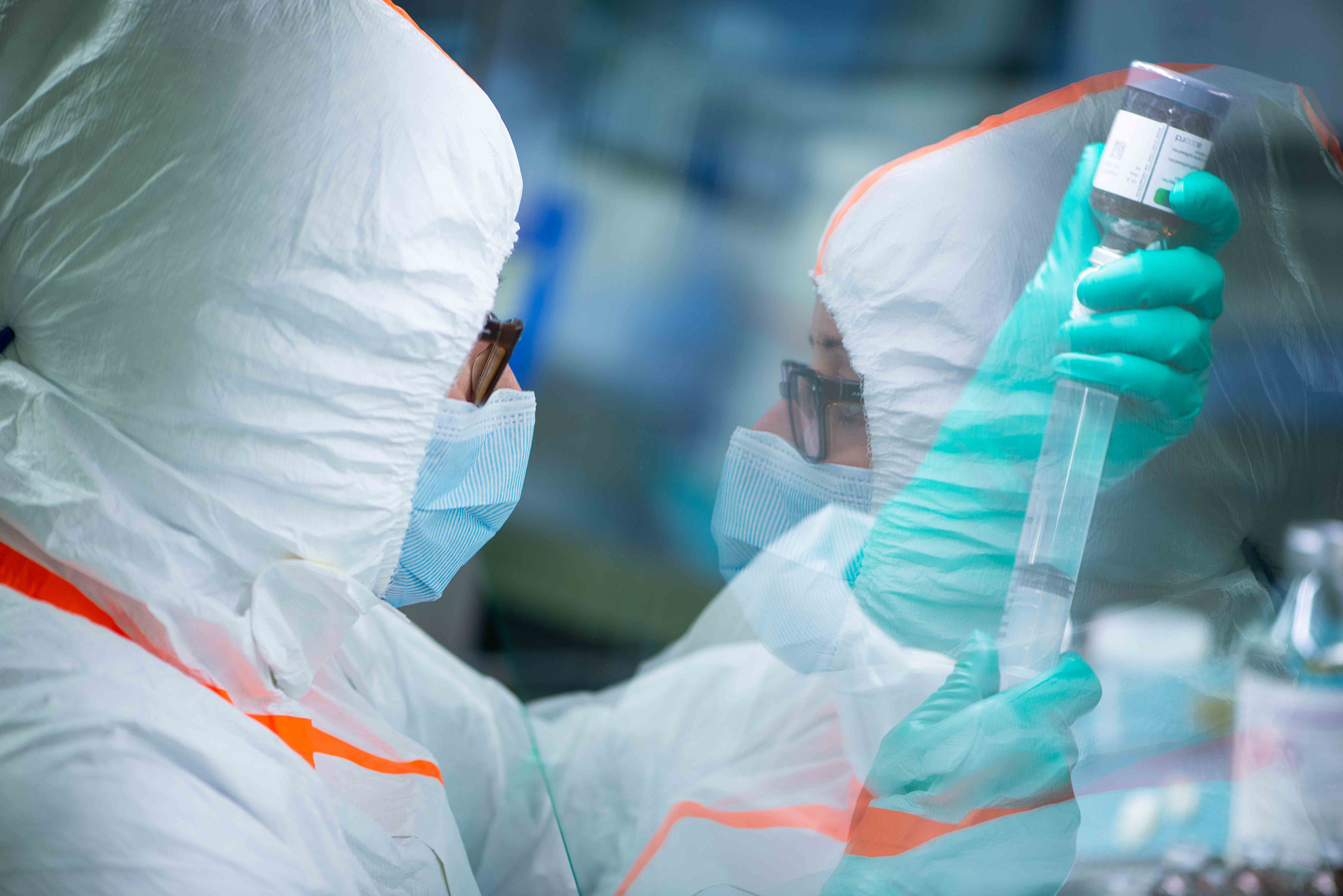 A woman wearing a face mask and special clothing holds utensils used to manufacture a drug.