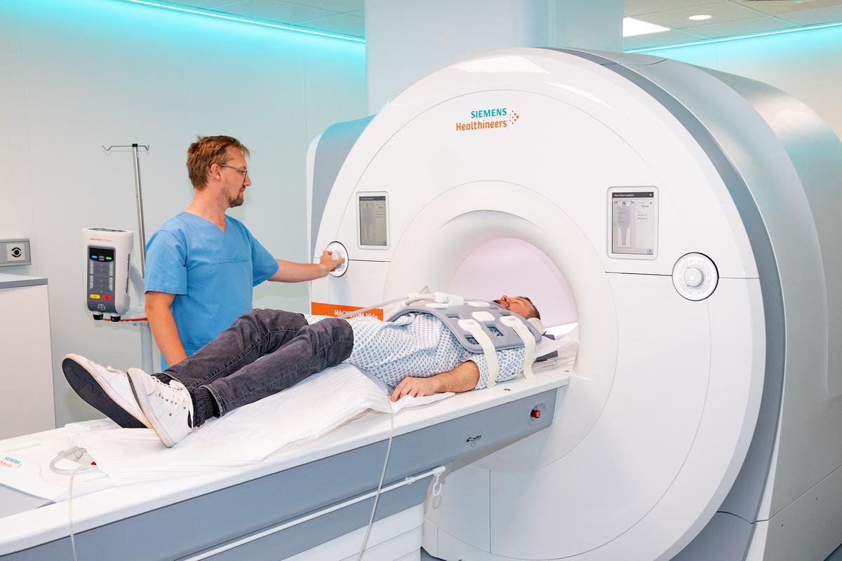 MHH radiologist Dr. Till Kaireit stands at an MRI scanner with a person lying on their back on the couch.