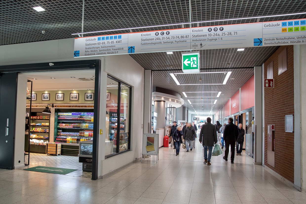 A view of the shopping arcade in the central MHH dormitory building. People are walking along the corridor, with shops to the right and left.