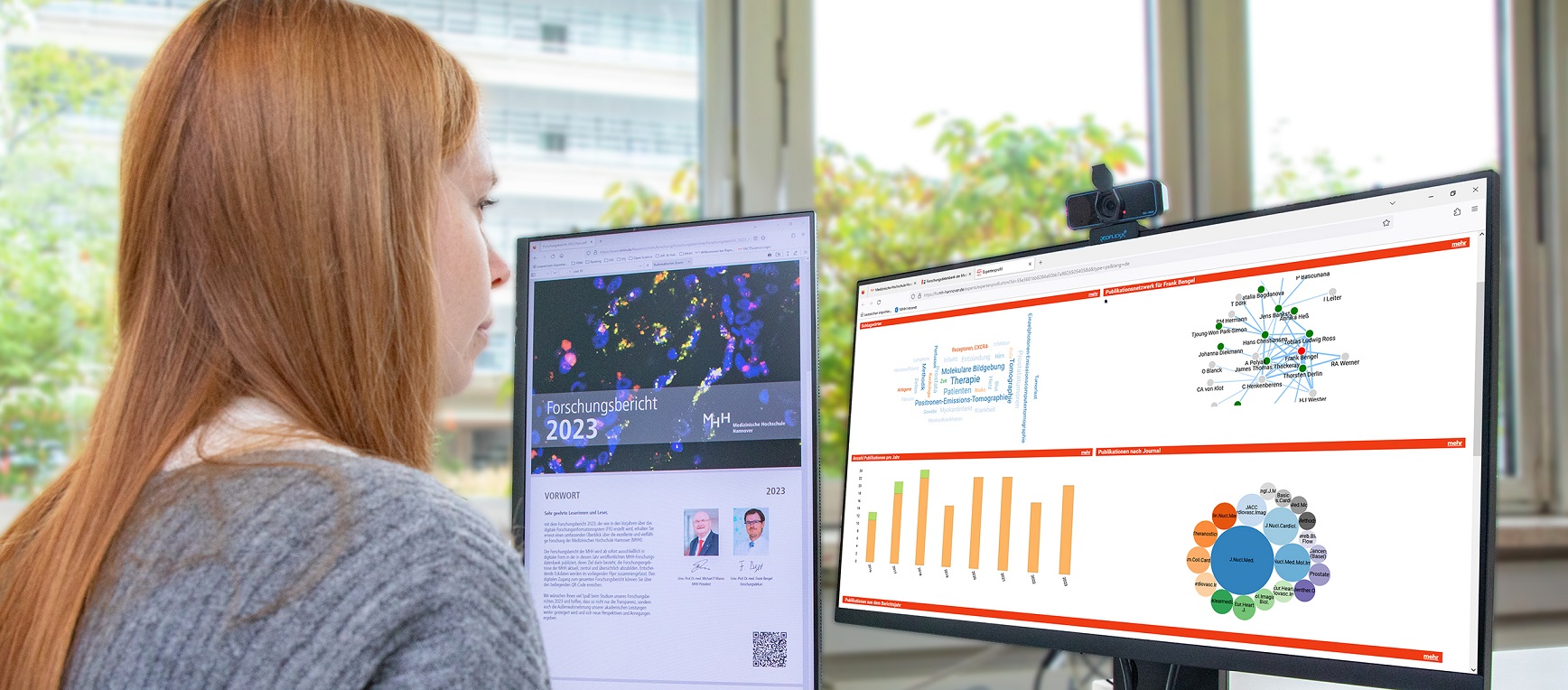 A woman is sitting at a desk in front of a PC monitor, which she is looking at.