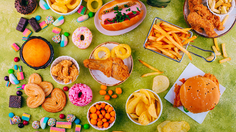  Many unhealthy foods such as doughnuts, chips, wine gums and burgers are served on a green surface. 