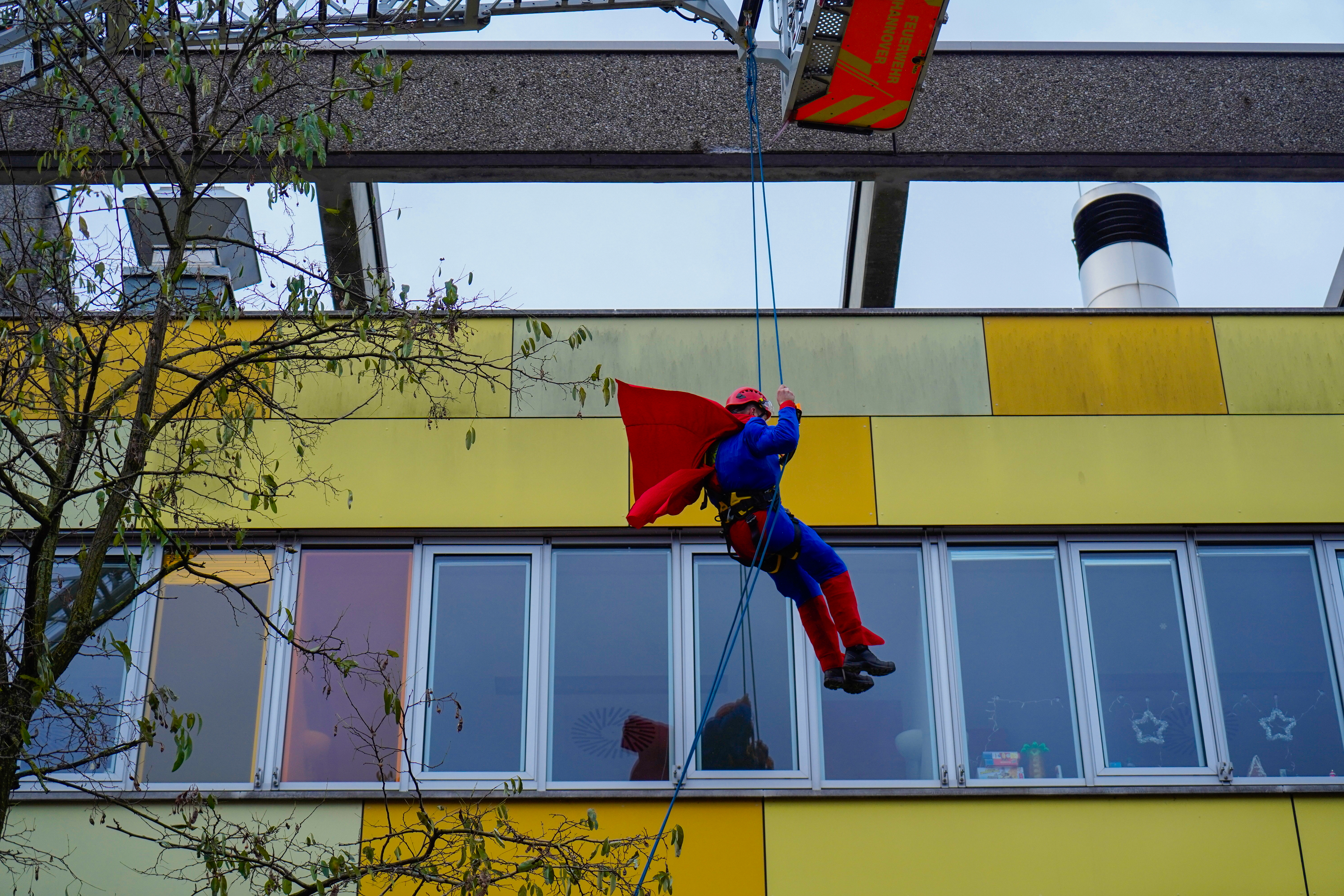 Ein Mann in Superman-Kostüm seilt sich an der Fassade der MHH-Kinderklinik ab. 