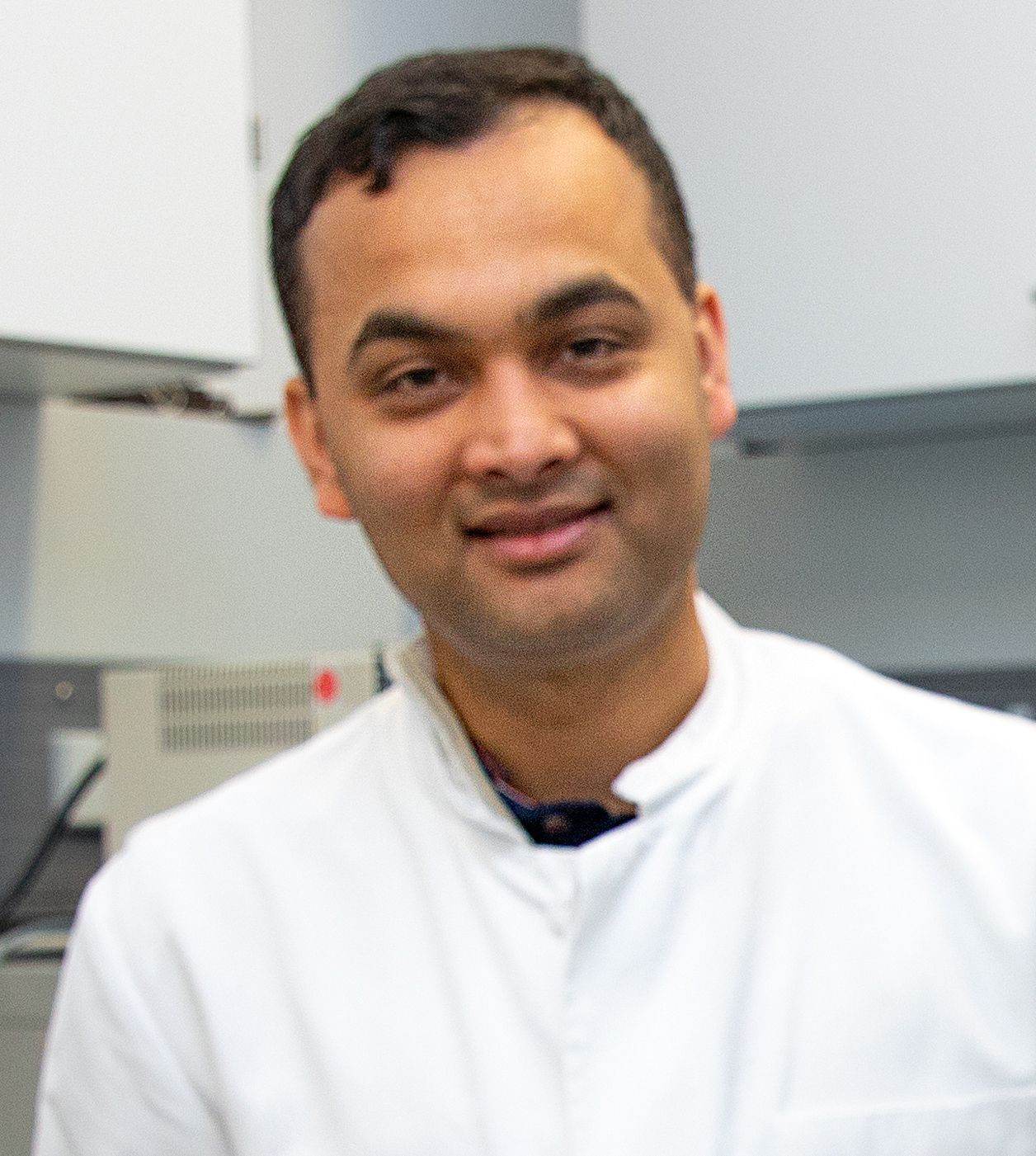 A man in a white coat is standing in a laboratory. 