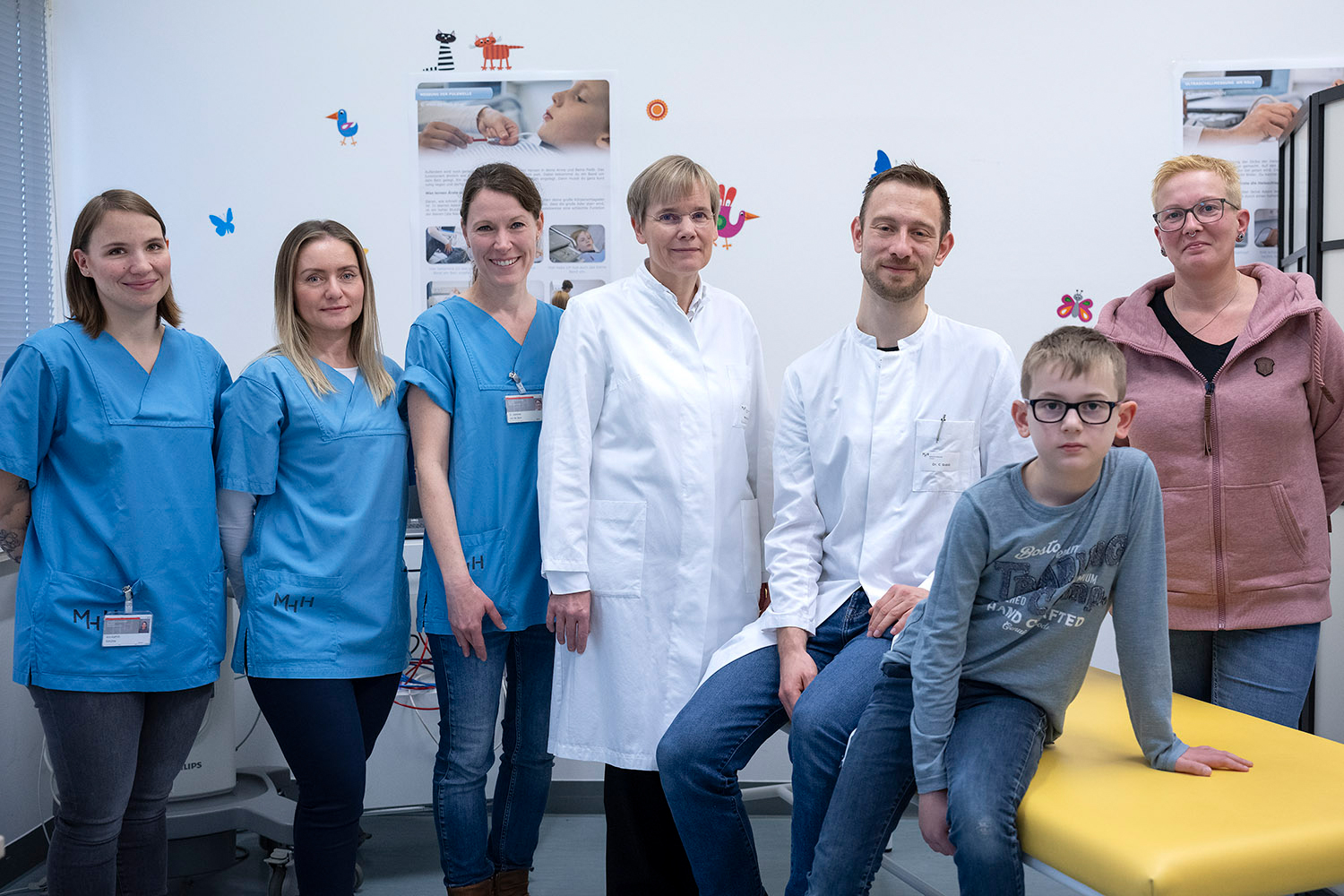 A ten-year-old boy sits on a treatment couch, surrounded by his mother and a study team.