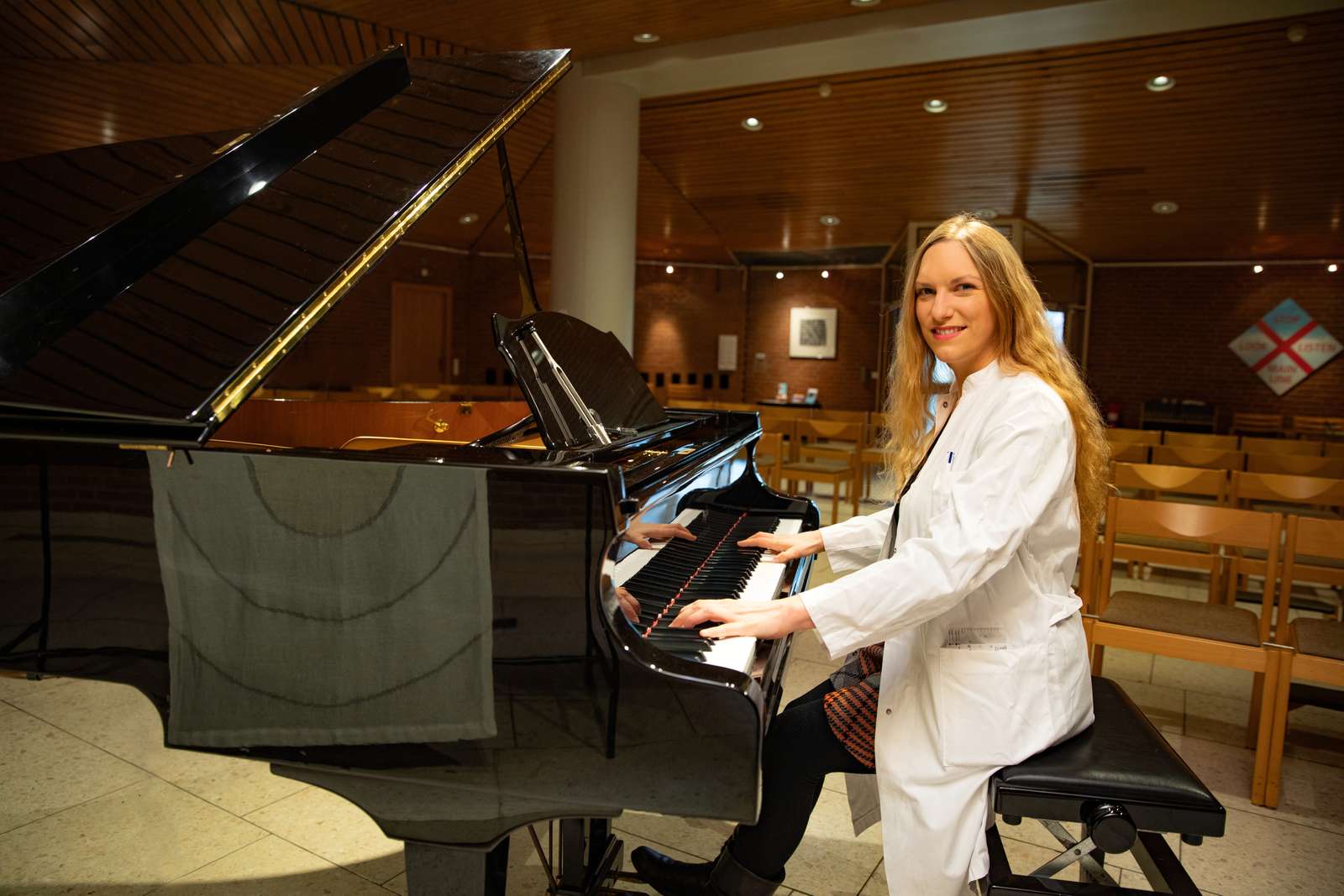  A woman in a white coat sits at a grand piano.