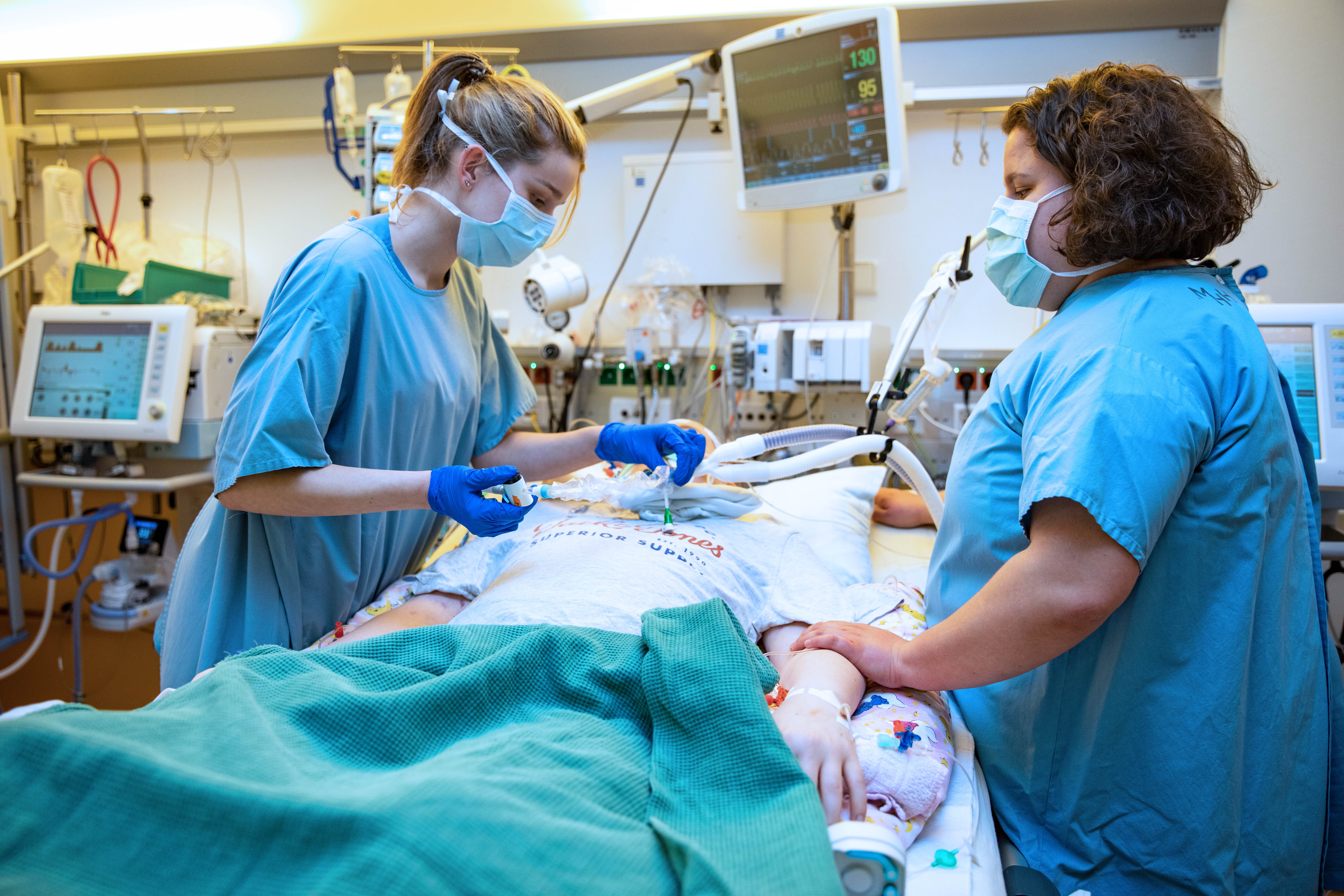 It shows two nursing staff in an intensive care unit at a patient's bedside