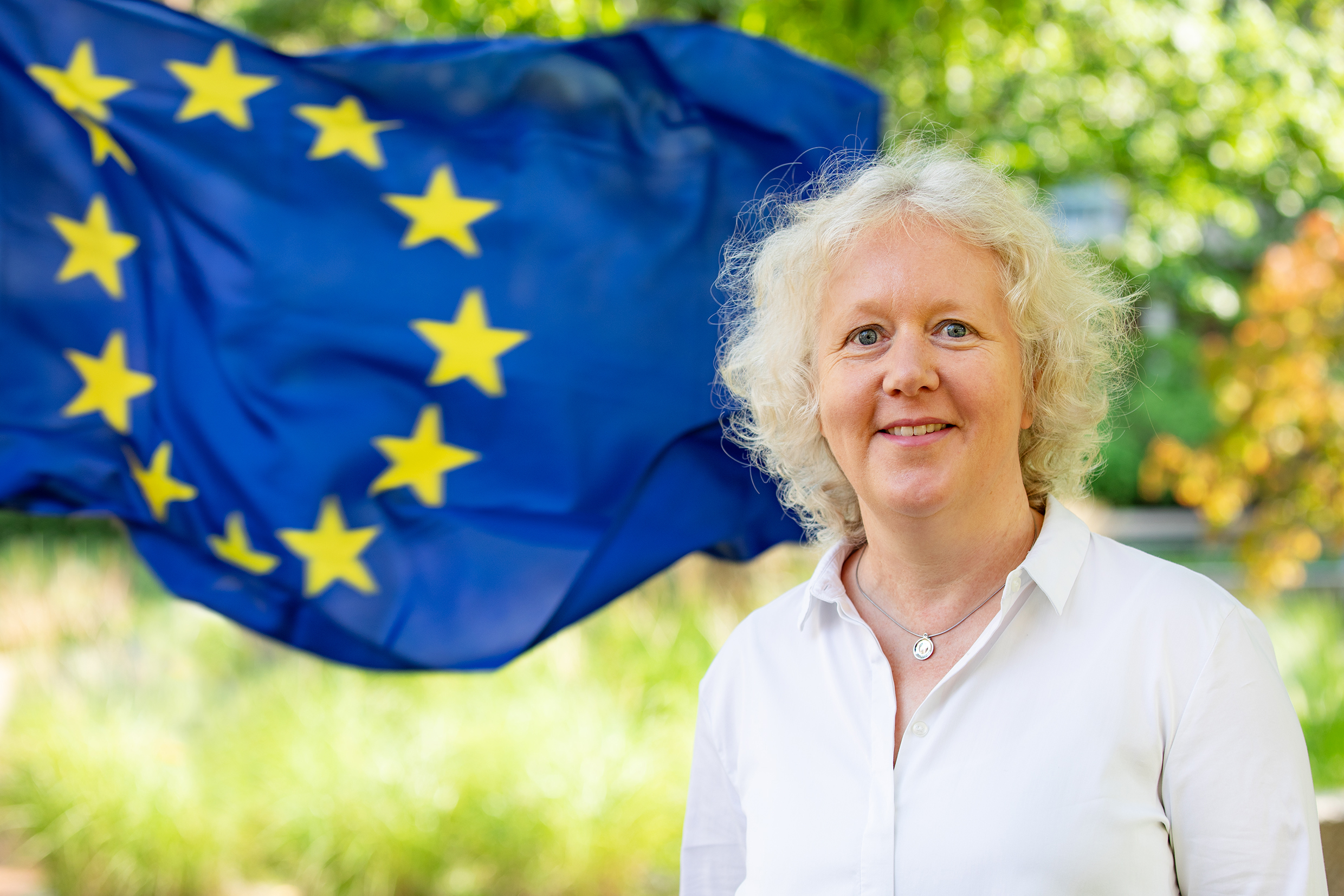 A woman stands in front of a European Union flag.