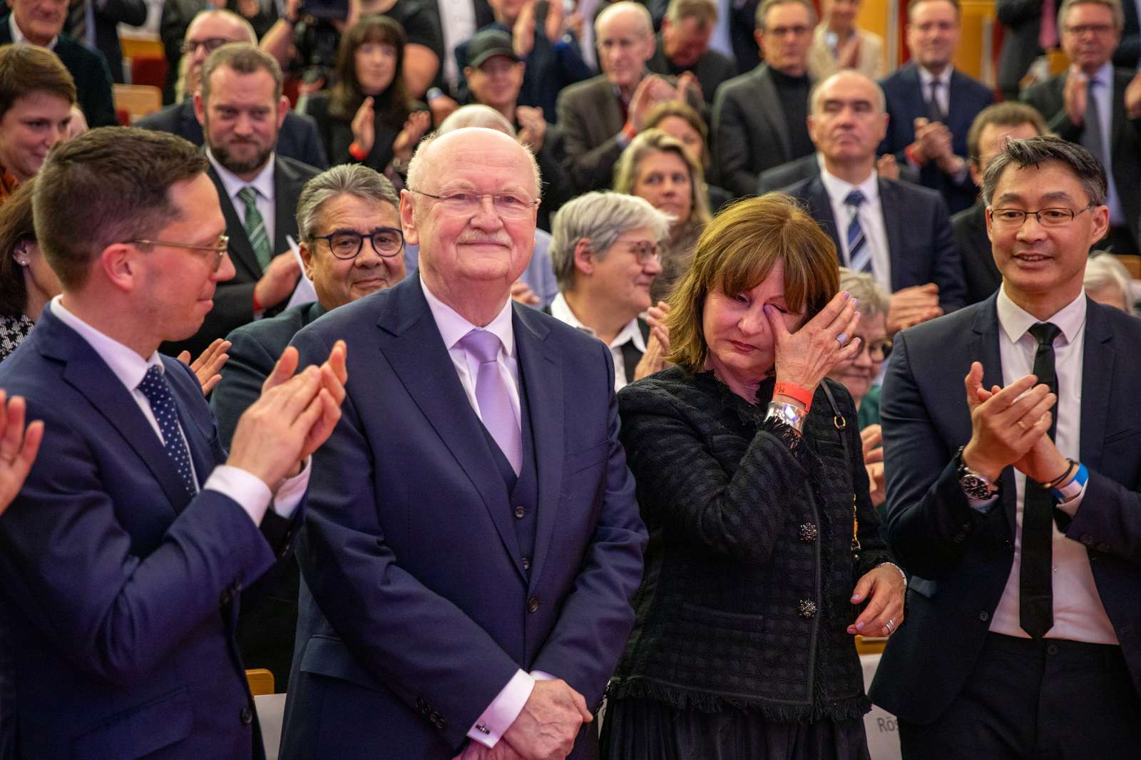 Professor Manns steht im vollem Hörsaal vorne, die Menschen um ihn herum applaudieren. 