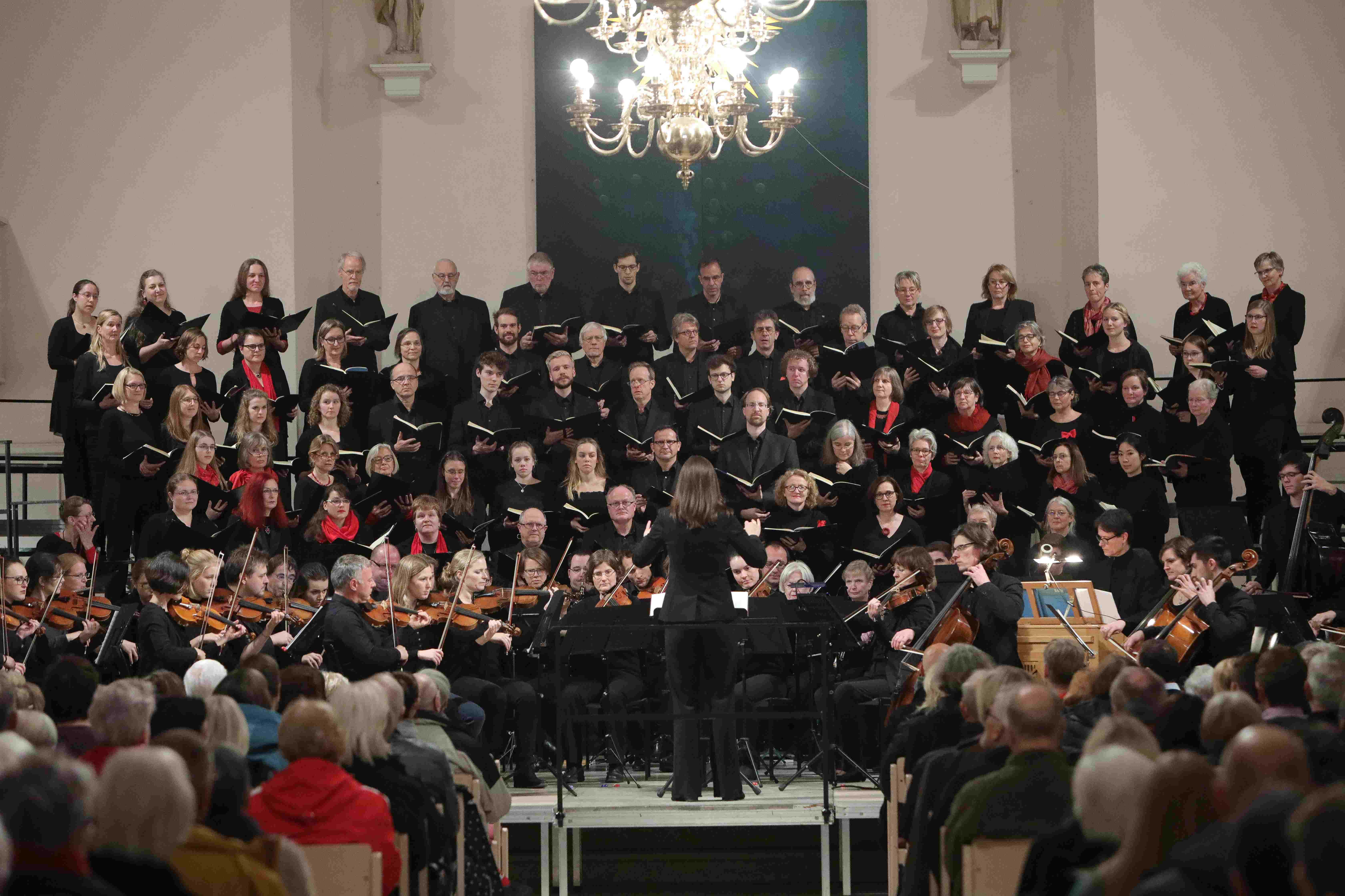 Chor der MHH steht in mehrreihigem Halbkreis, davor sitzt das Orchester