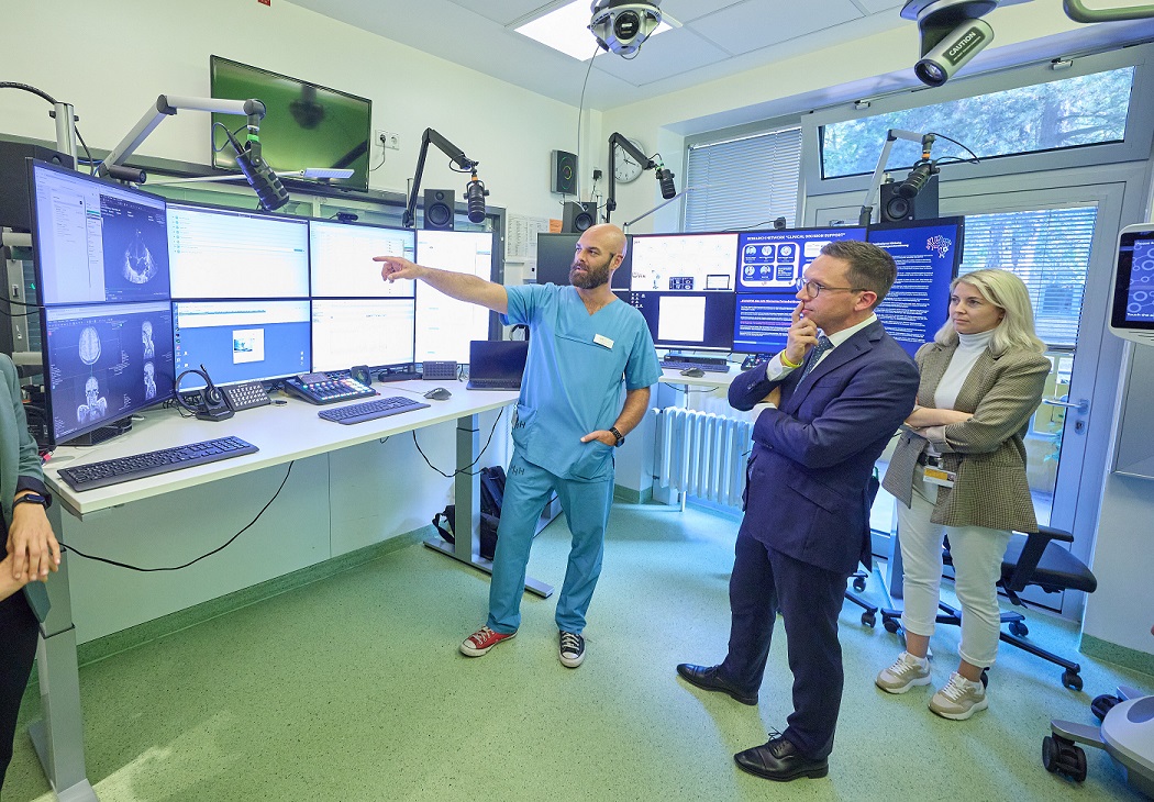 Minister Mohrs steht mit zwei weiteren Personen vor mehreren Monitoren. Eine Person in Kasack zeigt auf einen der Monitore.