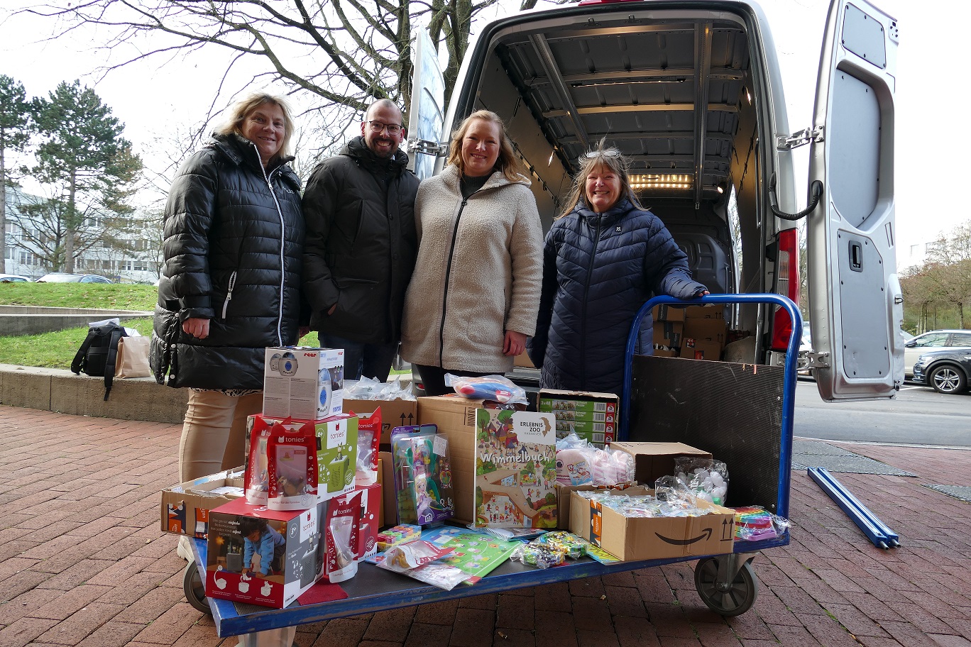 Vier Personen stehen vor einem Transportwagen voll mit eingepackten Geschenken. 